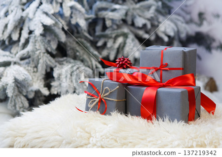 Christmas gifts decorated with red ribbon bows on soft fluffy carpet at blurred snowy fir tree background, closeup, selective focus. Winter holidays concept 137219342