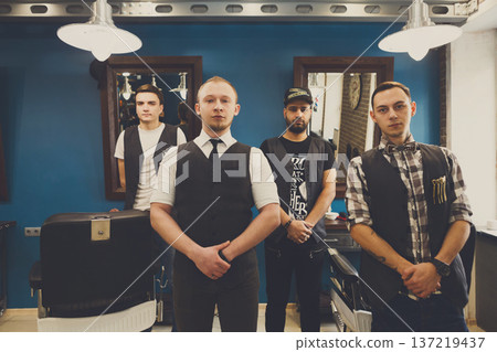 Team of barbers in modern barbershop. Four masculine male hairstylists standing indoors at workplace in hair salon Team of barbers in modern barbershop. Four masculine male hairstylists standing indoors at workplace in hair salon 137219437