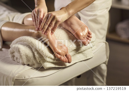 Therapist performing relaxing foot and leg massage at spa with warm oil and towels Therapist performing relaxing foot and leg massage at spa with warm oil and towels 137219519