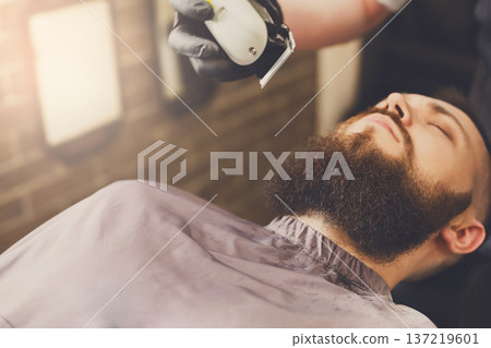 Barber styling beard with trimmer at barbershop, closeup. Stylish hairdresser in male hair salon 137219601