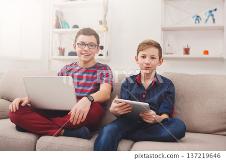 Children with devices - two cute teenagers using tablet and laptop while sitting on the couch in living room at home 137219646