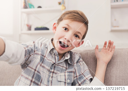 Happy child taking selfie for social networks. Boy at home on sofa in living room 137219715