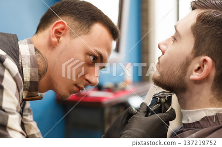 Stylish hairdresser in male hair salon. Barber styling beard with trimmer at barbershop, closeup. 137219752