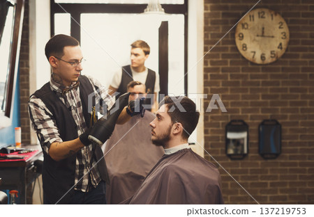 Man getting haircut by hairstylist at barbershop. Stylish barber and client 137219753