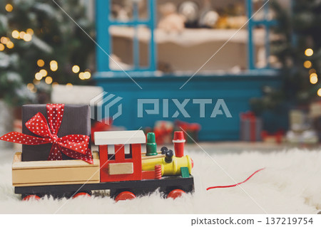 Wooden toy train with christmas gift on snowy decorated background. Selective focus, copy space Wooden toy train with christmas gift on snowy decorated background. Selective focus, copy space 137219754