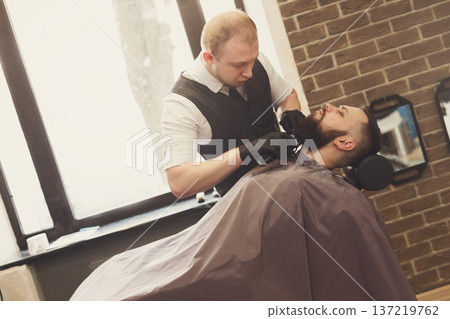 Barber styling beard with trimmer at barbershop, closeup. Hairdressing salon for men 137219762