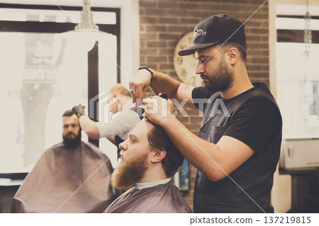 Man getting haircut by hairstylist at barbershop. Stylish barber and client 137219815