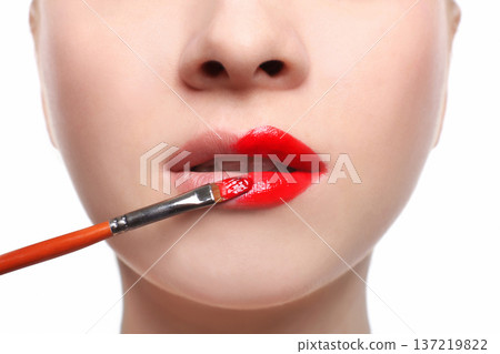 Lips closeup. Make-up artist apply lipstick with brush. Close-up of female model face with fashion glossy red makeup, beauty concept 137219822