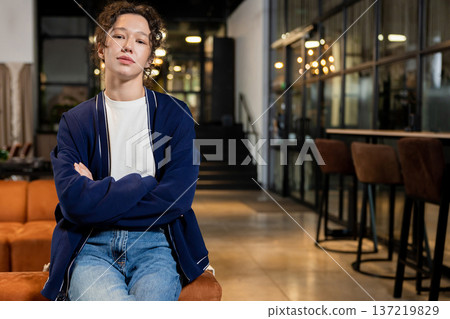 Calm woman seated on orange sofa looking friendly at camera in coworking interior 137219829