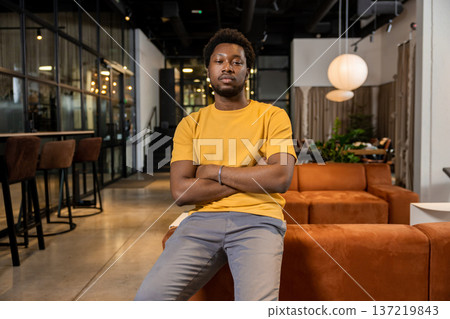 Serious male professional sitting on orange sofa arms crossed in coworking interior 137219843