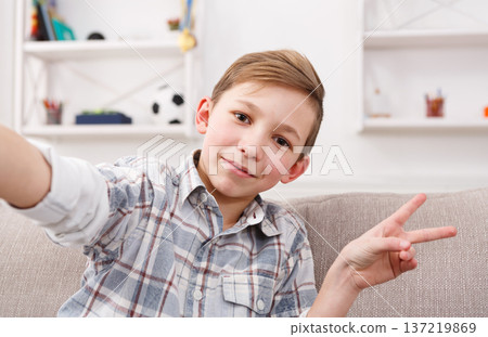 Happy child making selfie for social networks. Boy at home on sofa in living room Happy child making selfie for social networks. Boy at home on sofa in living room 137219869