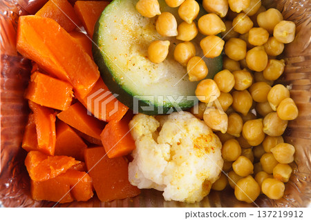 A vibrant meal box features orange carrots, green zucchini slices, creamy cauliflower, and yellow chickpeas, offering a colorful and nutritious selection perfect for a wholesome lunch or dinner. 137219912