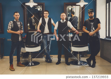 Team of barbers in modern barbershop. Four masculine male hairstylists standing indoors at workplace in hair salon 137219933