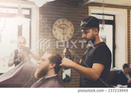 Man getting haircut by hairstylist at barbershop. Stylish barber and client 137219949