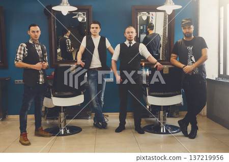 Team of barbers in modern barbershop. Four masculine male hairstylists standing indoors at workplace in hair salon Team of barbers in modern barbershop. Four masculine male hairstylists standing indoors at workplace in hair salon 137219956