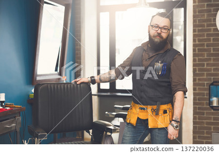Experienced bearded barber at workplace in barbershop. Professional stylish hairdresser waiting for client at hair salon Experienced bearded barber at workplace in barbershop. Professional stylish hairdresser waiting for client at hair salon 137220036
