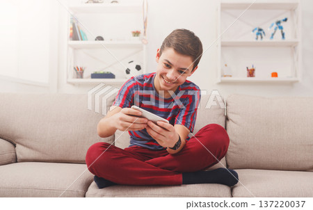Teenager playing games on smartphone with excitement while sitting on comfortable couch at home Teenager playing games on smartphone with excitement while sitting on comfortable couch at home 137220037