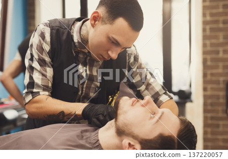 Barber styling beard to client at barbershop. Stylish hairdresser in male hair salon Barber styling beard to client at barbershop. Stylish hairdresser in male hair salon 137220057
