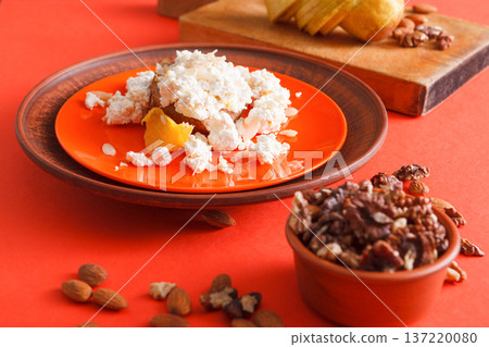 Healthy breakfast, dieting and detox concept - fresh cottage cheese on plate, bowl with nuts and wood board with fruit on bright background. Still life, selective focus. 137220080