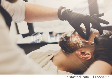 Barber styling beard with razor at barbershop, closeup. Stylish hairdresser in male hair salon 137220086