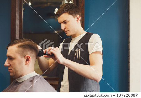 Barber makes male haircut in barbershop. Getting modern hairstyle in hair salon Barber makes male haircut in barbershop. Getting modern hairstyle in hair salon 137220087