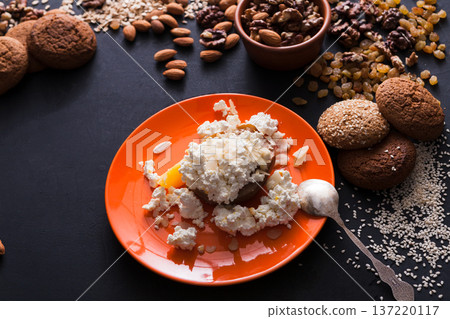 Healthy breakfast, dieting and detox concept - fresh cottage cheese on plate with nuts and oat cookies on dark background. Still life, selective focus, top view. 137220117