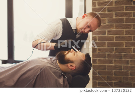 Barber styling beard to client at barbershop. Stylish hairdresser in male hair salon 137220122