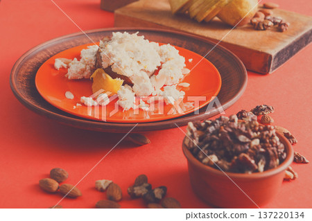 Healthy breakfast, dieting and detox concept - fresh cottage cheese on plate, bowl with nuts and wood board with fruit on bright background. Still life, selective focus. Healthy breakfast, dieting and detox concept - fresh cottage cheese on plate, bowl with nuts and wood board with fruit on bright background. Still life, selective focus. 137220134