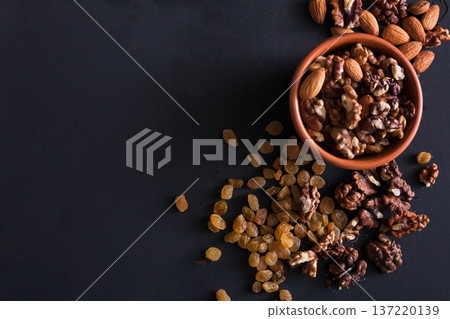 Nuts and raisins snack at black background. Healthy source of fat for vegans and vegetarians. Closeup, selective focus on almonds and copy space Nuts and raisins snack at black background. Healthy source of fat for vegans and vegetarians. Closeup, selective focus on almonds and copy space 137220139