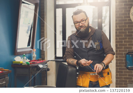 Experienced bearded barber at workplace in barbershop. Professional stylish hairdresser waiting for client at hair salon Experienced bearded barber at workplace in barbershop. Professional stylish hairdresser waiting for client at hair salon 137220159
