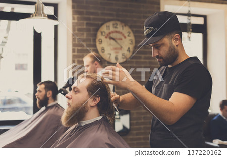 Barbers work in barbershop with bearded clients. Making modern hairstyle in male hair salon Barbers work in barbershop with bearded clients. Making modern hairstyle in male hair salon 137220162