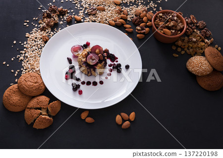 Healthy eating, dieting and detox concept - wholegrain fresh oatmeal porridge with fruits, berries, oat cookies and nuts on dark background. Healthy eating, dieting and detox concept - wholegrain fresh oatmeal porridge with fruits, berries, oat cookies and nuts on dark background. 137220198