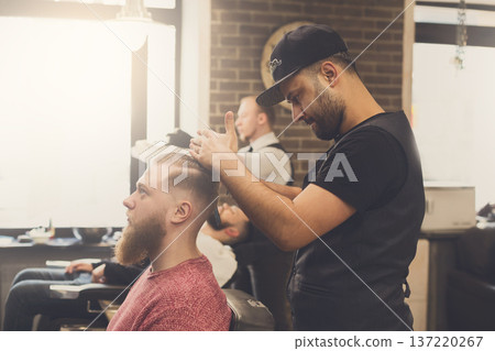 Male barbershop candid image. Styling beard to client. Stylish hairdressers in men hair salon 137220267