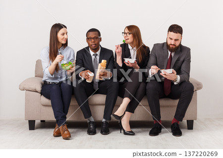 Business people eating, talking and smiling while having lunch sitting on couch in modern office, copy space 137220269