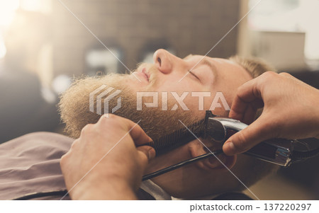 Barber styling beard at barbershop, closeup. Stylish hairdresser in male hair salon cutting hair with scissors Barber styling beard at barbershop, closeup. Stylish hairdresser in male hair salon cutting hair with scissors 137220297