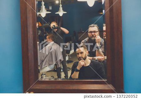 Man look at haircut by hairstylist at barbershop. Stylish barber and client in mirror Man look at haircut by hairstylist at barbershop. Stylish barber and client in mirror 137220352