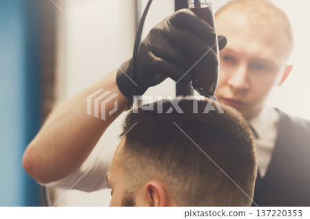 Man getting haircut with trimmer by hairstylist at barbershop. Modern hair salon 137220353