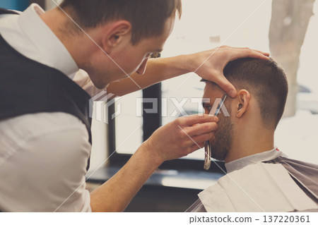Barber styling beard with razor at barbershop, closeup. Stylish hairdresser in male hair salon Barber styling beard with razor at barbershop, closeup. Stylish hairdresser in male hair salon 137220361
