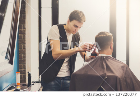 Barbers cuts hair in barbershop. Making modern hairstyle in male hair salon 137220377