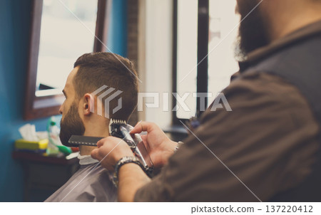 Barber make haircut with hair clipper in barbershop, closeup of client's head. Stylish hairdresser in male hair salon Barber make haircut with hair clipper in barbershop, closeup of client's head. Stylish hairdresser in male hair salon 137220412