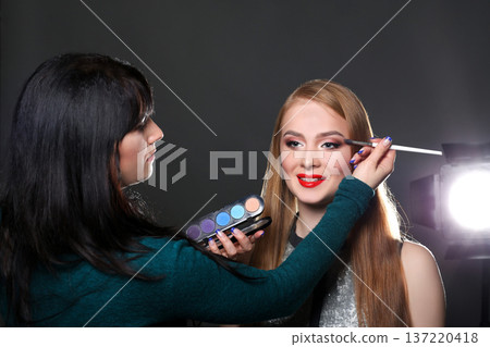 Make-up artist working with beauty model, applying eyeshadow palette, dark studio background Make-up artist working with beauty model, applying eyeshadow palette, dark studio background 137220418