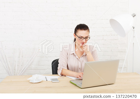 Middle aged businesswoman working in white modern office interior, with laptop. Female office work, woman in eye glasses, pensive and concentrated. High key, soft tone. woman in office. Middle aged businesswoman working in white modern office interior, with laptop. Female office work, woman in eye glasses, pensive and concentrated. High key, soft tone. woman in office. 137220470