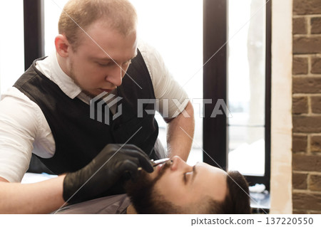 Barber in barbershop make beard haircut. Hairstyle in male hair salon Barber in barbershop make beard haircut. Hairstyle in male hair salon 137220550
