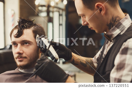 Barber make haircut with hair clipper in barbershop, closeup of client's head. Stylish hairdresser in male hair salon Barber make haircut with hair clipper in barbershop, closeup of client's head. Stylish hairdresser in male hair salon 137220551