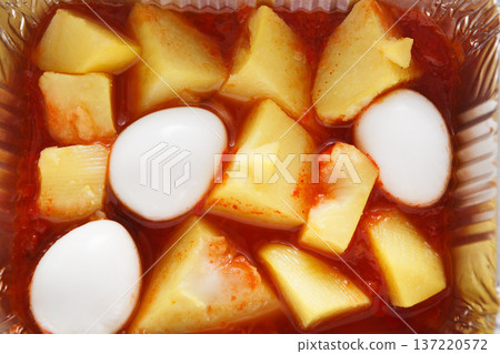 Chunks of yellow potatoes and white boiled eggs are scattered in a vibrant red sauce. This dish showcases a mix of textures and flavors, appearing appetizing and ready to taste. Chunks of yellow potatoes and white boiled eggs are scattered in a vibrant red sauce. This dish showcases a mix of textures and flavors, appearing appetizing and ready to taste. 137220572