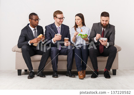 Business people eating, talking and smiling while having lunch sitting on couch in modern office, copy space 137220582