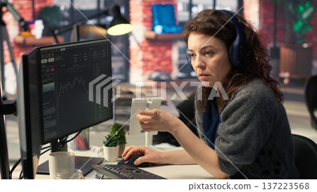 Female day trader examines stock market graphs on dual monitors, tracking financial growth to share prices. Trading interface provides real time data for buying and selling shares. Camera B. Female day trader examines stock market graphs on dual monitors, tracking financial growth to share prices. Trading interface provides real time data for buying and selling shares. Camera B. 137223568