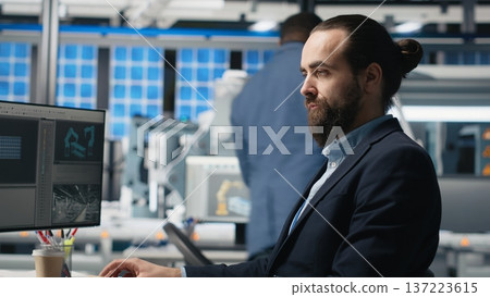 Professional engineer reviewing insight on pc at the solar panels plant, conducting an inspection to ensure alternative energy systems for production line and development goals. Camera B. 137223615