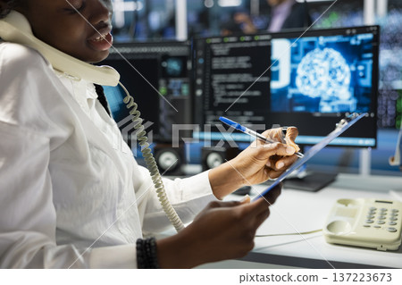 Close up of data center operator taking notes while talking in phone call, providing user technical support. Server famr employee answering telephone calls , noting customer requests Close up of data center operator taking notes while talking in phone call, providing user technical support. Server famr employee answering telephone calls , noting customer requests 137223673