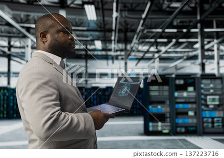 Server hub system administrator using AI software on laptop to monitor equipment energy consumption. IT professional managing supercomputers in server hub using artificial intelligence tech Server hub system administrator using AI software on laptop to monitor equipment energy consumption. IT professional managing supercomputers in server hub using artificial intelligence tech 137223716